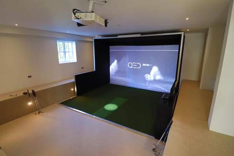 Moderner Indoor Golf Simulator mit Projektionsfläche und Abschlagmatte in hellem Raum