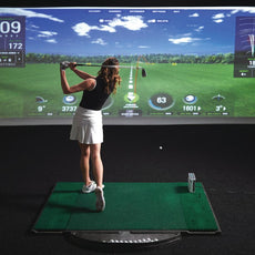 Frau spielt Golf im Indoor Golf Simulator mit digitaler Anzeige und Golfmatte