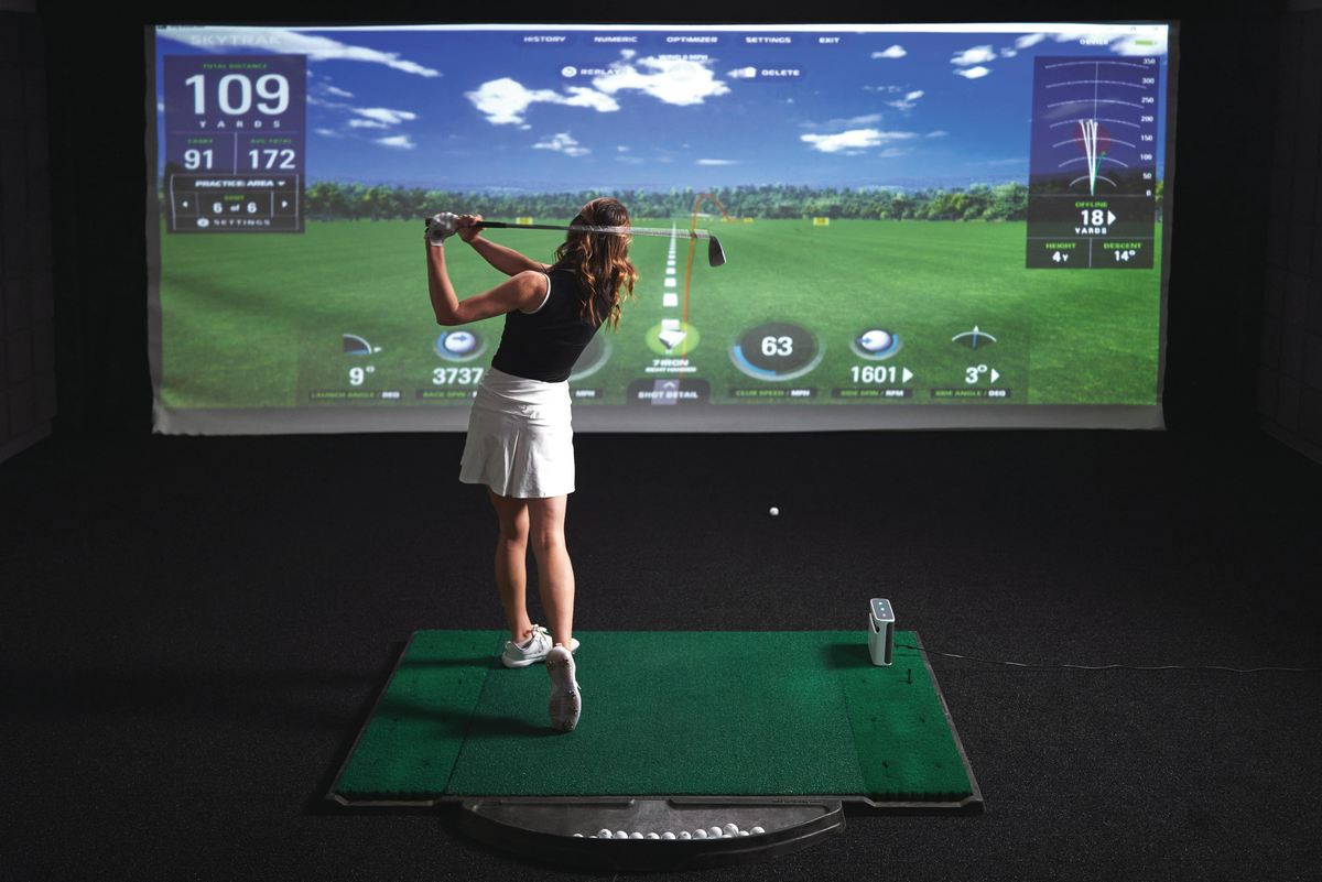 Frau spielt Golf im Indoor Golf Simulator mit digitaler Anzeige und Golfmatte