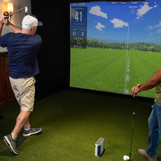 Zwei Männer spielen Golf auf einem Indoor-Golfsimulator mit großem Bildschirm und Golfschlägern.