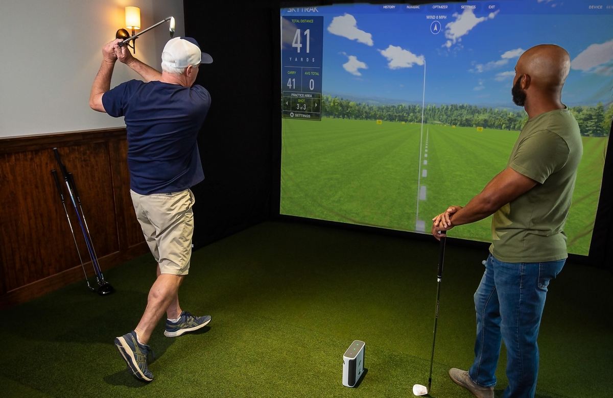 Zwei Männer spielen Golf auf einem Indoor-Golfsimulator mit großem Bildschirm und Golfschlägern.
