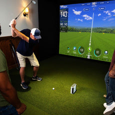 Drei Männer nutzen einen modernen Golf Simulator mit großem Bildschirm und Golfschläger im Indoor-Bereich.