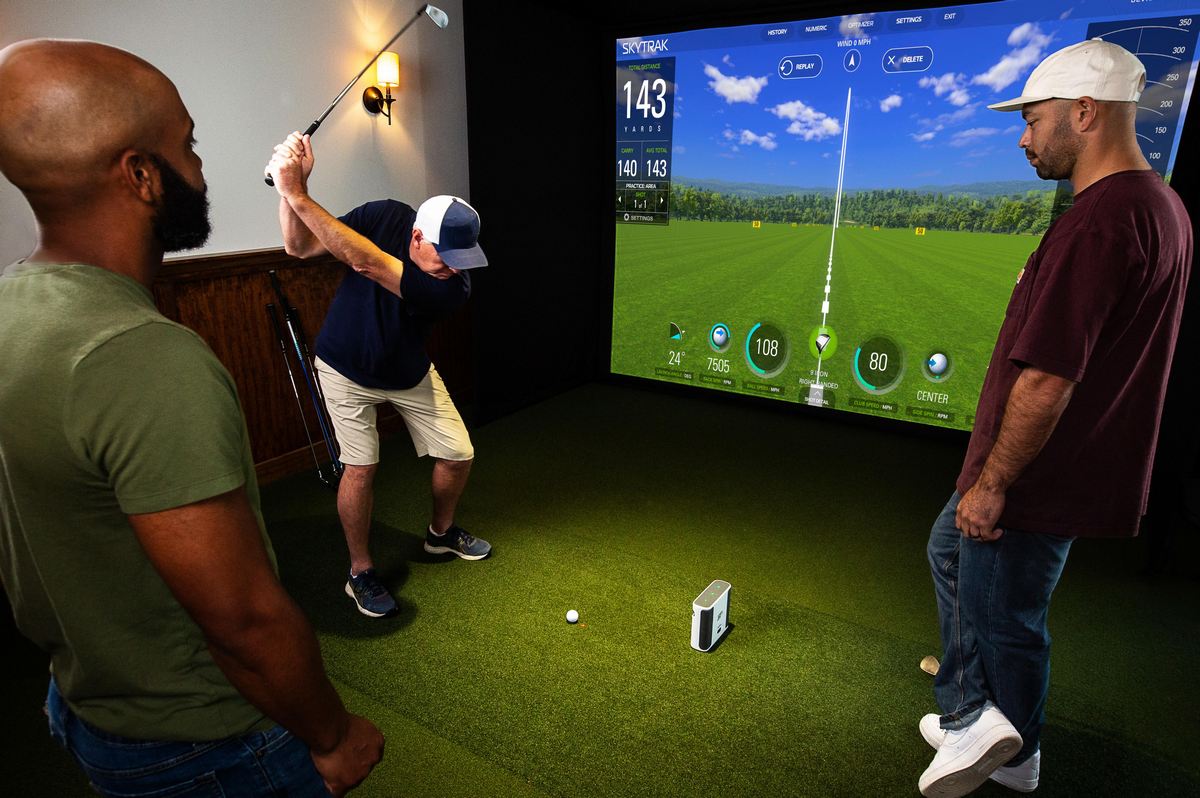 Drei Männer nutzen einen modernen Golf Simulator mit großem Bildschirm und Golfschläger im Indoor-Bereich.