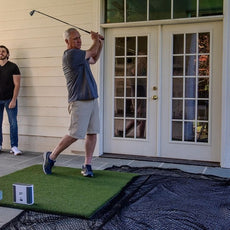 Mann übt Golfabschlag mit Golf Simulator und Netz auf Terrasse, Golfausrüstung Outdoor