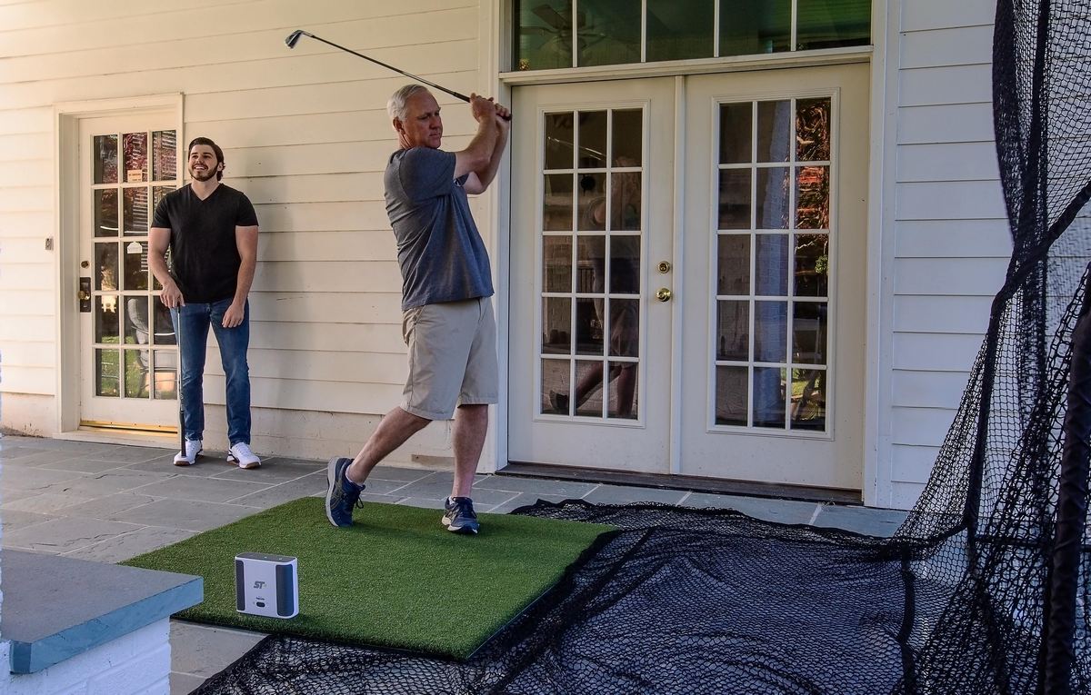 Mann übt Golfabschlag mit Golf Simulator und Netz auf Terrasse, Golfausrüstung Outdoor