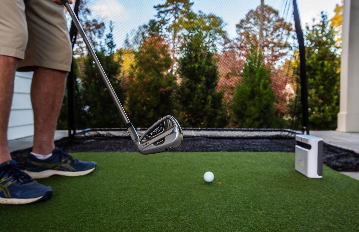 Golfspieler mit Eisen schlägt Golfball im Garten, Outdoor-Golfnetz und Golf Simulator