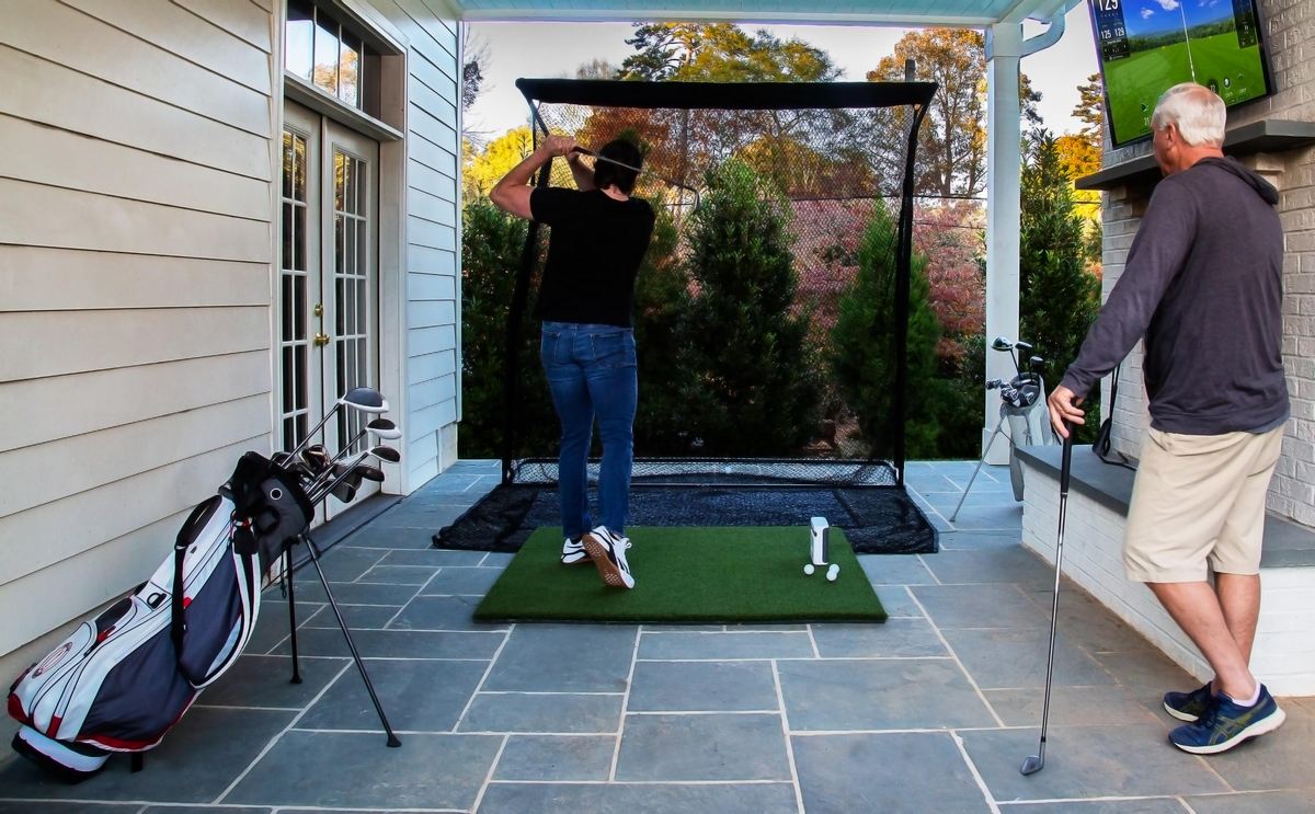 Golf Simulator Outdoor-Set mit Netz, Golfschläger und zwei Personen auf Terrasse