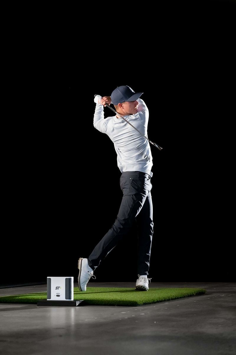 Golfspieler beim Abschlag auf Indoor-Golfmatte mit Golf Simulator und Launch Monitor