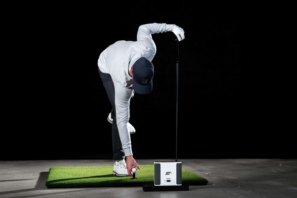 Golfer platziert Ball auf Abschlagmatte vor Golf Simulator und Launch Monitor, Indoor Golf Szene