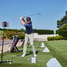 Golfer beim Abschlag auf Driving Range mit Golfbällen, Golftasche und Golf Simulator Outdoor