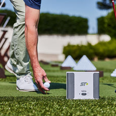 Golfspieler platziert Golfball neben Golf Launch Monitor Rapsodo ST+ auf Driving Range mit Golfschläger