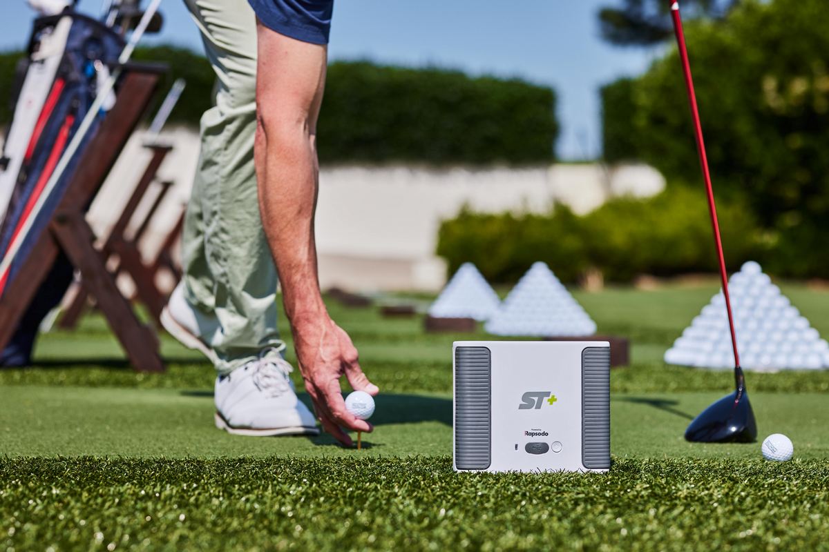 Golfspieler platziert Golfball neben Golf Launch Monitor Rapsodo ST+ auf Driving Range mit Golfschläger