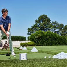 Golfspieler beim Abschlag auf Driving Range mit Golfbällen, Golfmatte und Launch Monitor