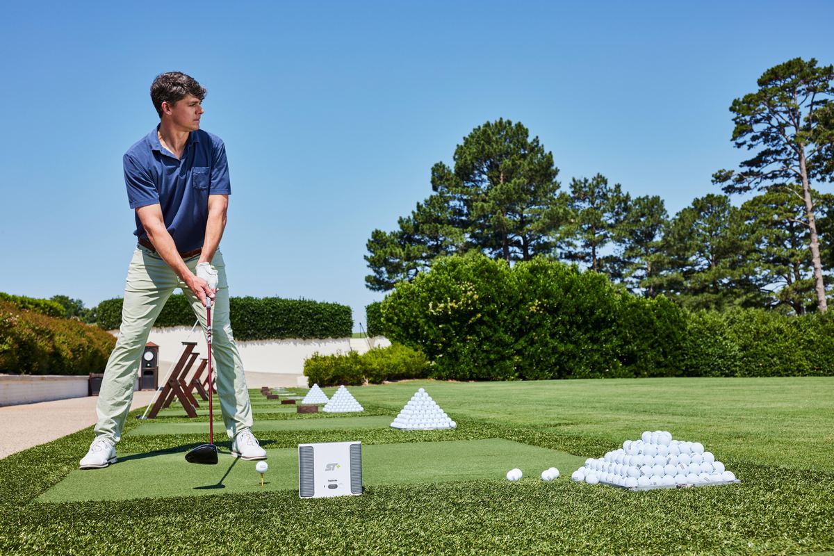 Golfspieler beim Abschlag auf Driving Range mit Golfbällen, Golfmatte und Launch Monitor