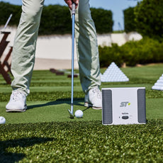 Golfspieler mit Golfball und Schläger auf Driving Range, Rapsodo SkyTrak+ Golf Launch Monitor im Vordergrund