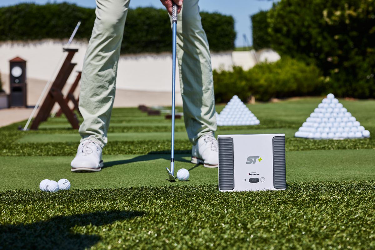 Golfspieler mit Golfball und Schläger auf Driving Range, Rapsodo SkyTrak+ Golf Launch Monitor im Vordergrund
