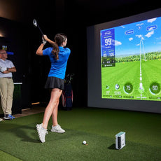 Golferin nutzt Indoor Golf Simulator, zwei Personen schauen zu, moderner Raum, großes Display