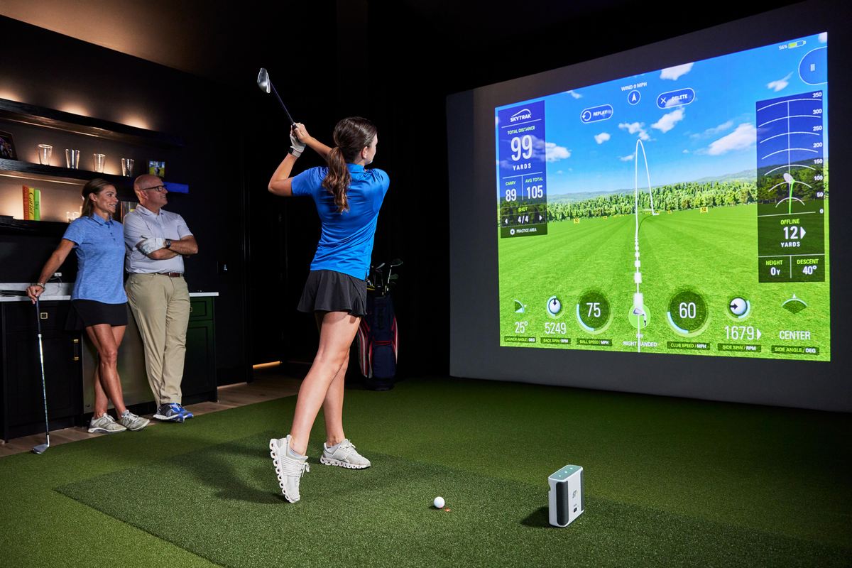 Golferin nutzt Indoor Golf Simulator, zwei Personen schauen zu, moderner Raum, großes Display