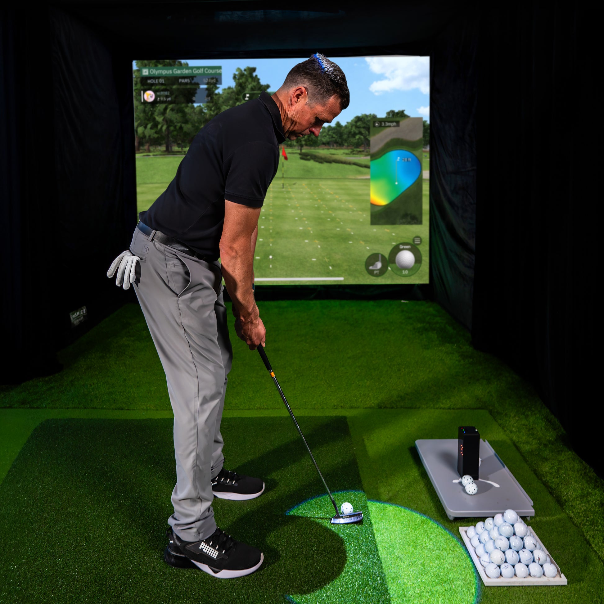 Golfer beim Putten im Indoor Golf Simulator, mit Golfbällen und Zubehör auf Kunstrasen