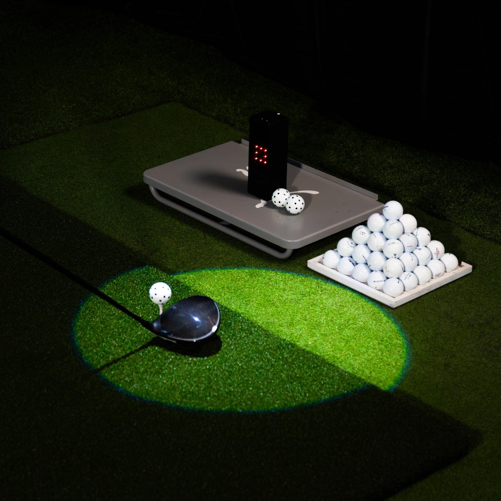 Golfballabschlag auf Kunstrasen mit Driver, Launch Monitor und Pyramide aus Golfbällen