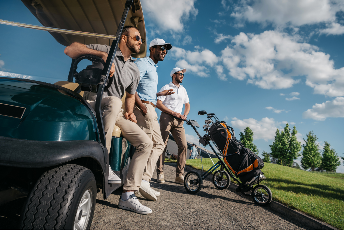 Gruppe von Freunden mit Golfwagen und Golfbags auf sonnigem Golfplatz, Golfzubehör sichtbar
